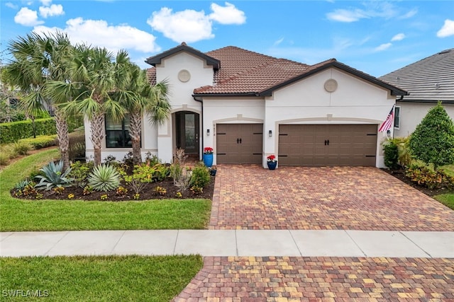 mediterranean / spanish house featuring a tiled roof, decorative driveway, an attached garage, and stucco siding