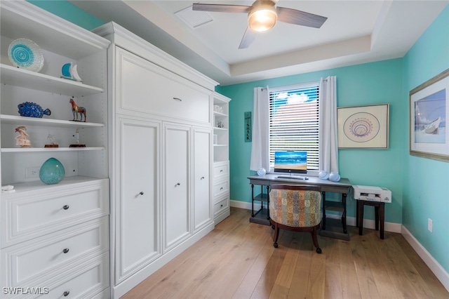 office area with light wood-style flooring, visible vents, baseboards, a ceiling fan, and a tray ceiling