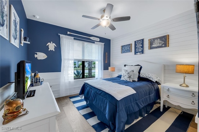 bedroom with light wood-type flooring, ceiling fan, and wooden walls