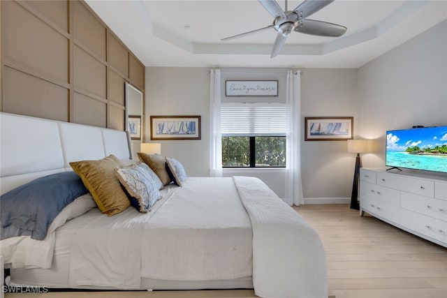 bedroom with ceiling fan, a raised ceiling, and light hardwood / wood-style flooring