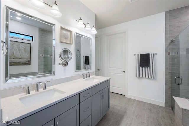 full bathroom featuring double vanity, a stall shower, a sink, and wood finished floors