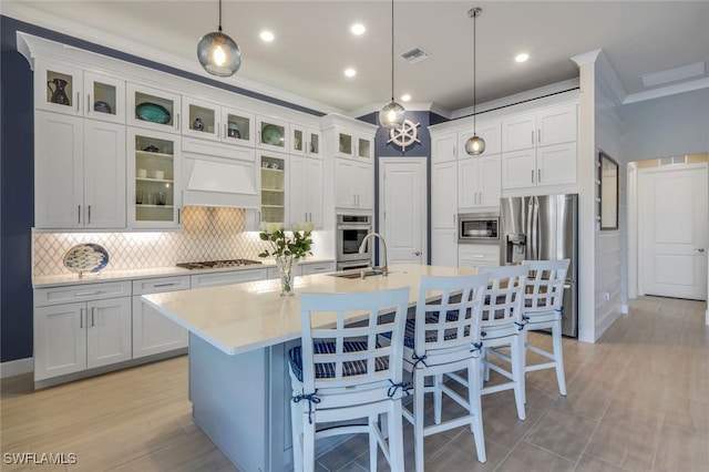 kitchen with premium range hood, crown molding, pendant lighting, a kitchen island with sink, and appliances with stainless steel finishes