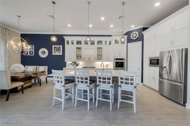 kitchen with stainless steel appliances, tasteful backsplash, an island with sink, decorative light fixtures, and white cabinets