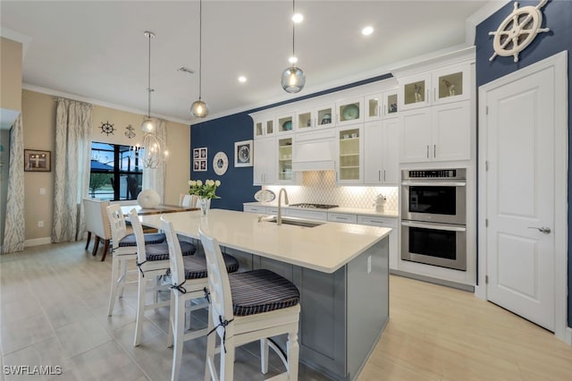 kitchen featuring backsplash, a center island with sink, sink, decorative light fixtures, and white cabinetry