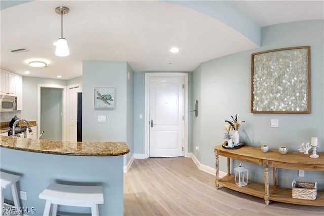 kitchen featuring hanging light fixtures, light hardwood / wood-style flooring, dark stone countertops, white cabinetry, and kitchen peninsula