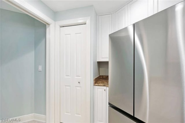 kitchen featuring white cabinets, stainless steel fridge, and stone counters