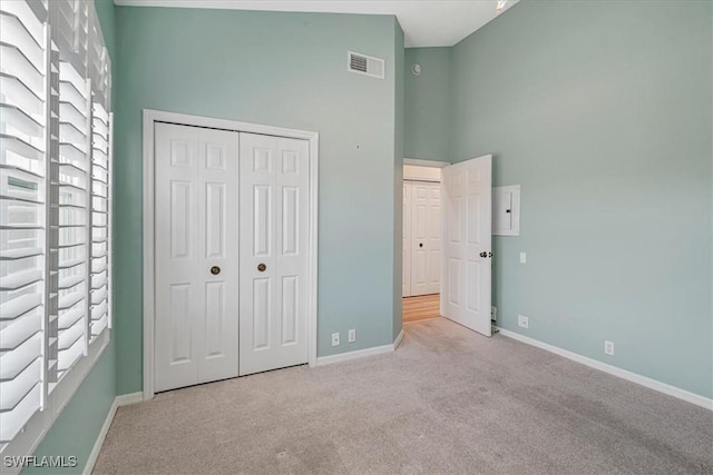 unfurnished bedroom featuring electric panel, light carpet, a high ceiling, and a closet