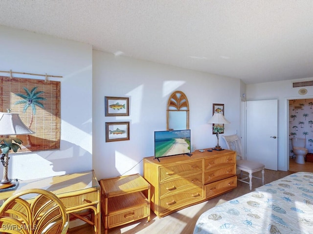 bedroom with connected bathroom, a textured ceiling, and hardwood / wood-style flooring