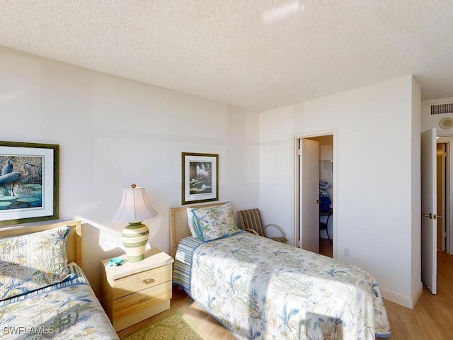 bedroom with light wood-type flooring, a textured ceiling, a walk in closet, and a closet