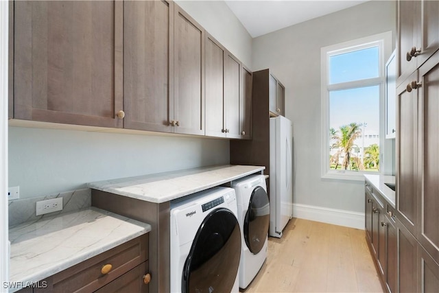 clothes washing area featuring washer and clothes dryer, plenty of natural light, cabinets, and light wood-type flooring