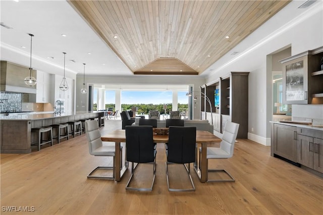 dining room with a raised ceiling, light hardwood / wood-style flooring, and wooden ceiling