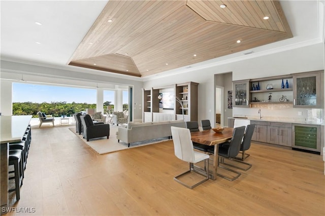 dining room featuring a tray ceiling, beverage cooler, light hardwood / wood-style flooring, wooden ceiling, and bar area