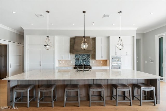 kitchen featuring white cabinets, custom range hood, a large island, and a breakfast bar area