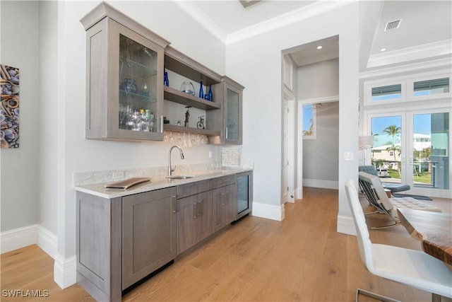 bar featuring sink, light hardwood / wood-style flooring, light stone countertops, ornamental molding, and beverage cooler