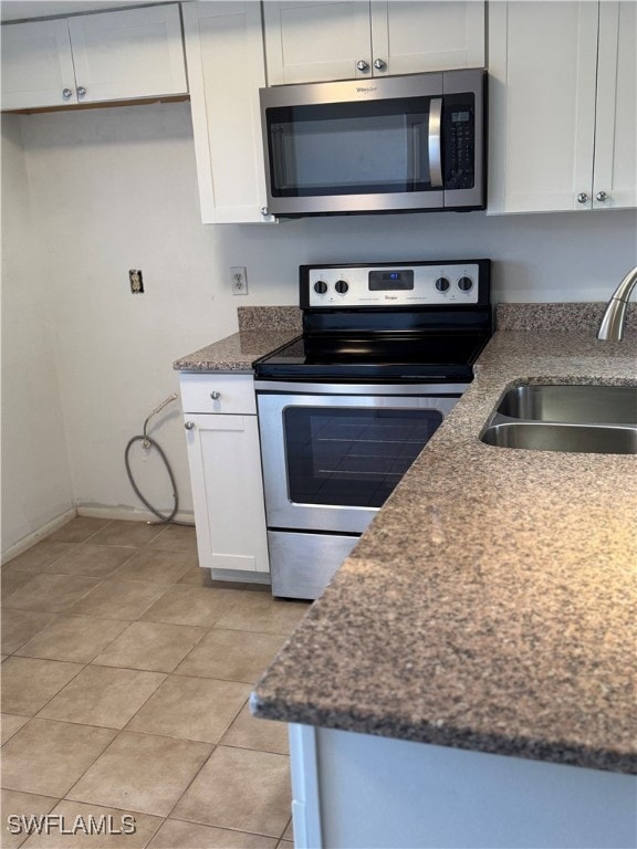 kitchen featuring stainless steel appliances, sink, dark stone countertops, white cabinetry, and light tile patterned flooring