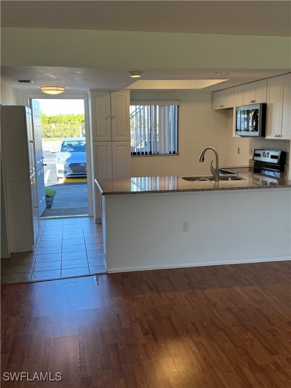 kitchen featuring kitchen peninsula, appliances with stainless steel finishes, white cabinetry, and wood-type flooring