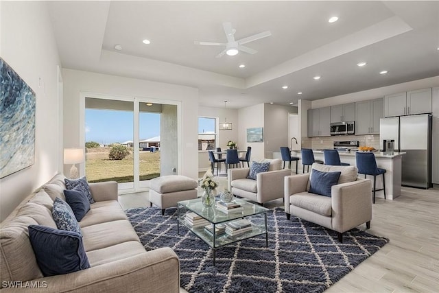 living room with ceiling fan, a raised ceiling, and light wood-type flooring