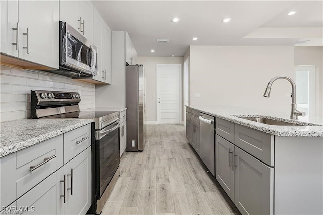 kitchen with light stone counters, sink, appliances with stainless steel finishes, and light hardwood / wood-style flooring