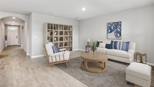 living room featuring light wood-type flooring, baseboards, arched walkways, and recessed lighting