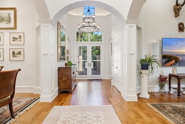 foyer entrance with french doors, ornamental molding, a towering ceiling, a notable chandelier, and light hardwood / wood-style floors