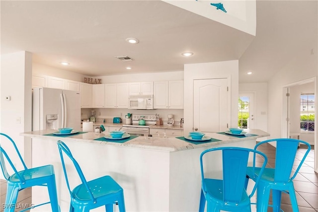 kitchen featuring white cabinets, light tile patterned floors, white appliances, and a kitchen breakfast bar