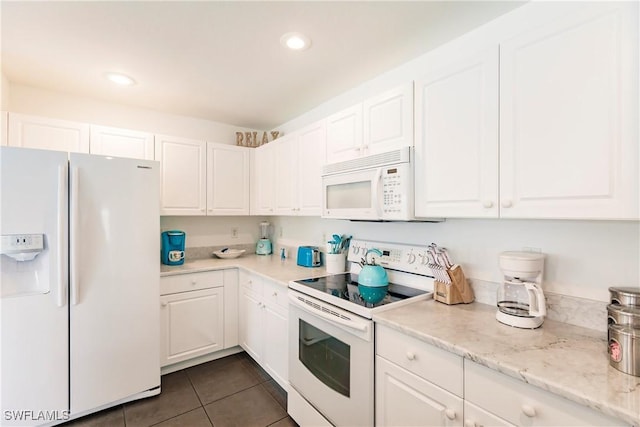 kitchen featuring white cabinets, white appliances, light stone counters, and dark tile patterned floors