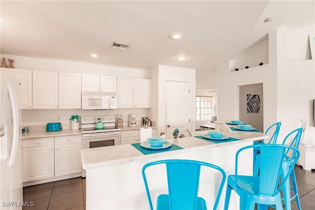 kitchen with dark tile patterned flooring, white cabinetry, white appliances, and a kitchen island with sink