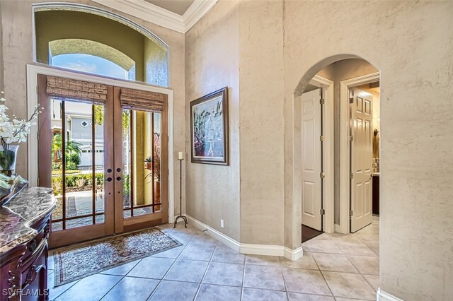 tiled foyer entrance featuring french doors, a towering ceiling, a wealth of natural light, and crown molding