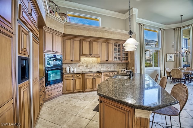 kitchen with light tile patterned floors, black double oven, crown molding, and an island with sink