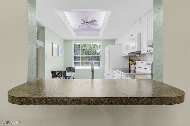 kitchen with a raised ceiling, decorative backsplash, white cabinets, and white appliances