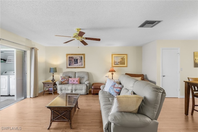 living room featuring washing machine and clothes dryer, a textured ceiling, and light hardwood / wood-style flooring