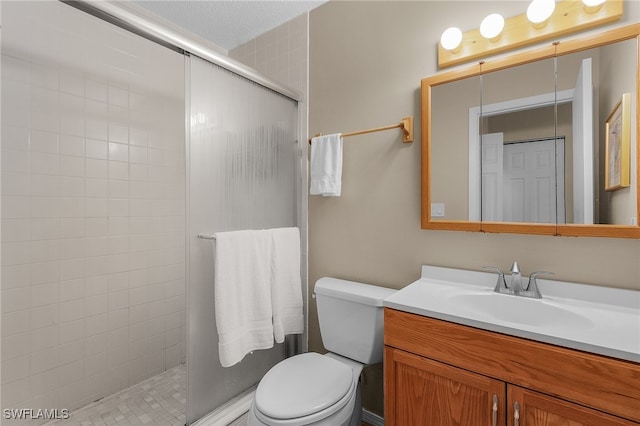 bathroom with vanity, toilet, a shower with shower door, and a textured ceiling