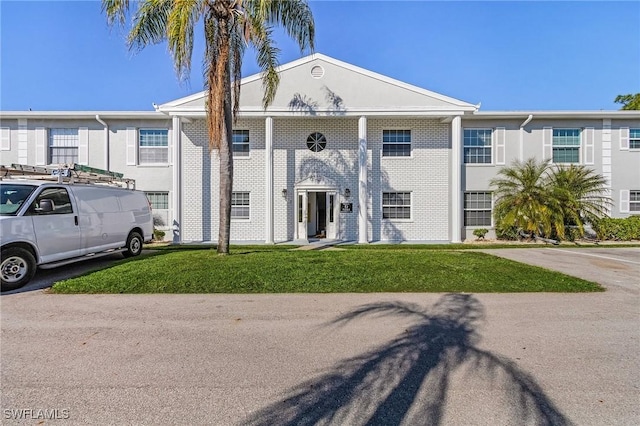 greek revival inspired property featuring a front lawn and brick siding