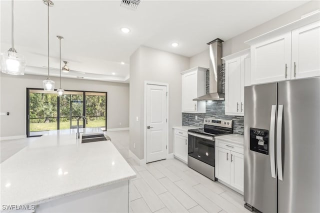 kitchen featuring white cabinetry, sink, wall chimney range hood, pendant lighting, and appliances with stainless steel finishes