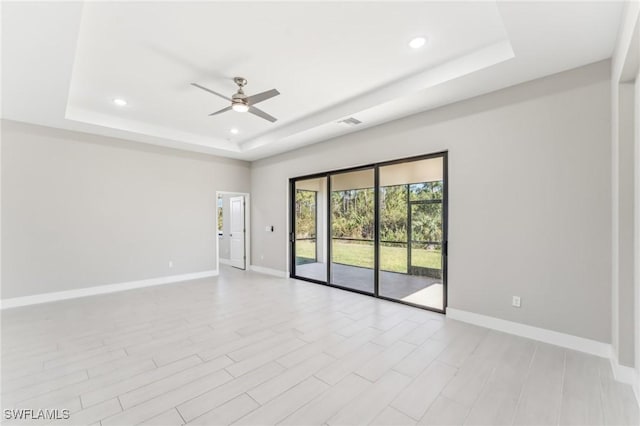 empty room with a raised ceiling, ceiling fan, and light wood-type flooring