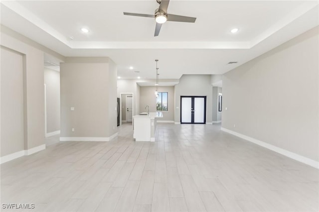 unfurnished living room featuring ceiling fan, french doors, sink, a raised ceiling, and light hardwood / wood-style flooring