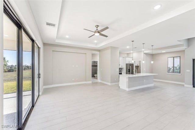 unfurnished living room featuring a tray ceiling, light hardwood / wood-style flooring, and ceiling fan