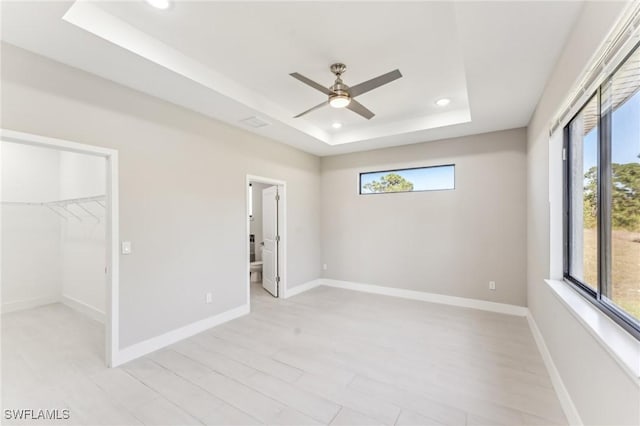 unfurnished bedroom featuring ensuite bath, a tray ceiling, ceiling fan, a spacious closet, and a closet