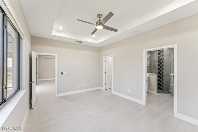 unfurnished room with a tray ceiling, ceiling fan, and light wood-type flooring