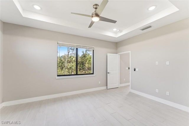 unfurnished room featuring a raised ceiling, ceiling fan, and light hardwood / wood-style floors