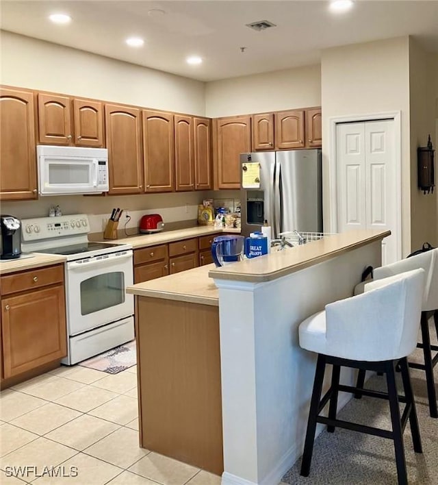 kitchen with a breakfast bar, a center island with sink, light tile patterned flooring, and white appliances