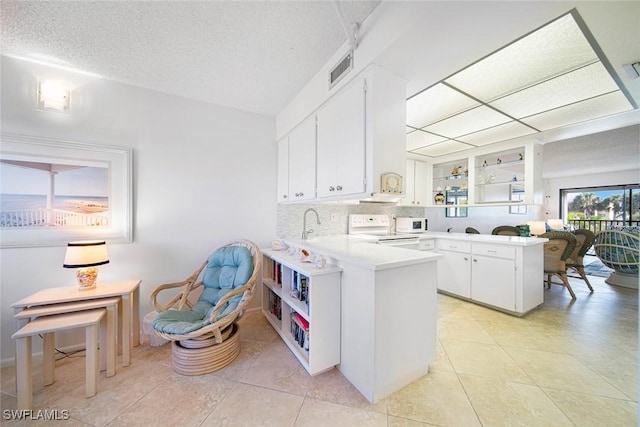 kitchen with white appliances, backsplash, white cabinets, light tile patterned flooring, and kitchen peninsula