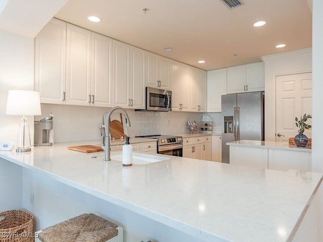 kitchen featuring stainless steel appliances, backsplash, kitchen peninsula, a breakfast bar area, and white cabinets