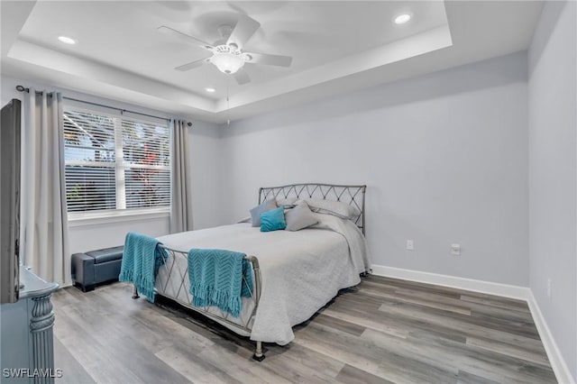 bedroom with a raised ceiling, ceiling fan, and hardwood / wood-style floors