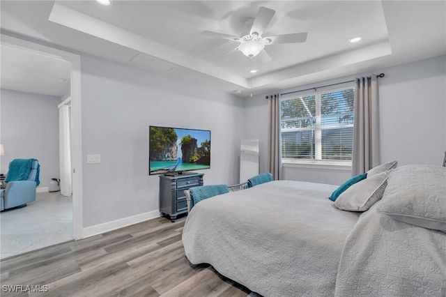 bedroom with ceiling fan, a raised ceiling, and light hardwood / wood-style flooring