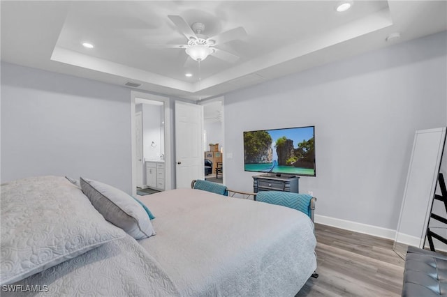 bedroom featuring a raised ceiling, ensuite bathroom, ceiling fan, and wood-type flooring