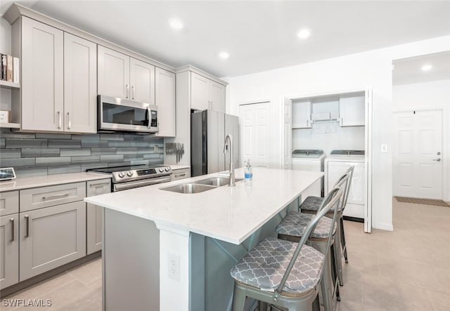 kitchen featuring separate washer and dryer, stainless steel appliances, gray cabinets, and a kitchen island with sink