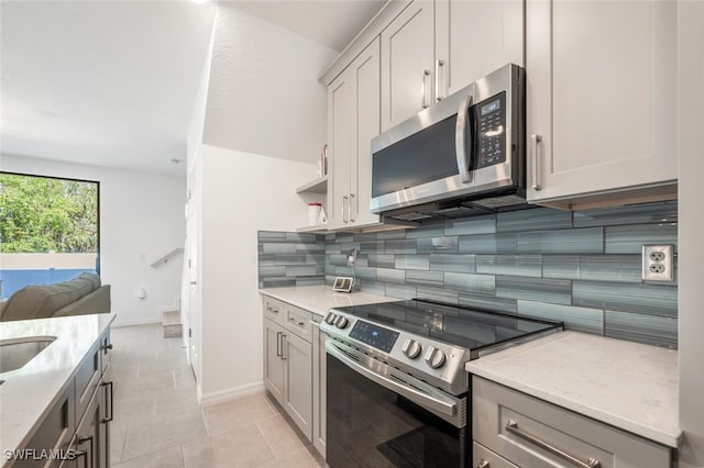 kitchen with light stone countertops, appliances with stainless steel finishes, tasteful backsplash, gray cabinetry, and light tile patterned flooring