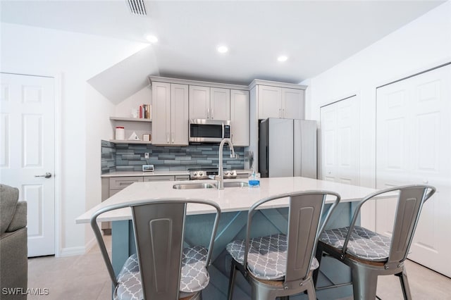 kitchen with gray cabinetry, tasteful backsplash, a center island with sink, and fridge