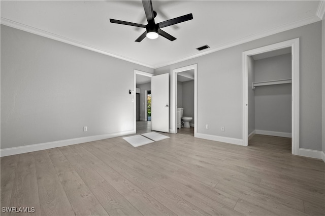 unfurnished bedroom featuring a walk in closet, light hardwood / wood-style flooring, ceiling fan, ornamental molding, and connected bathroom